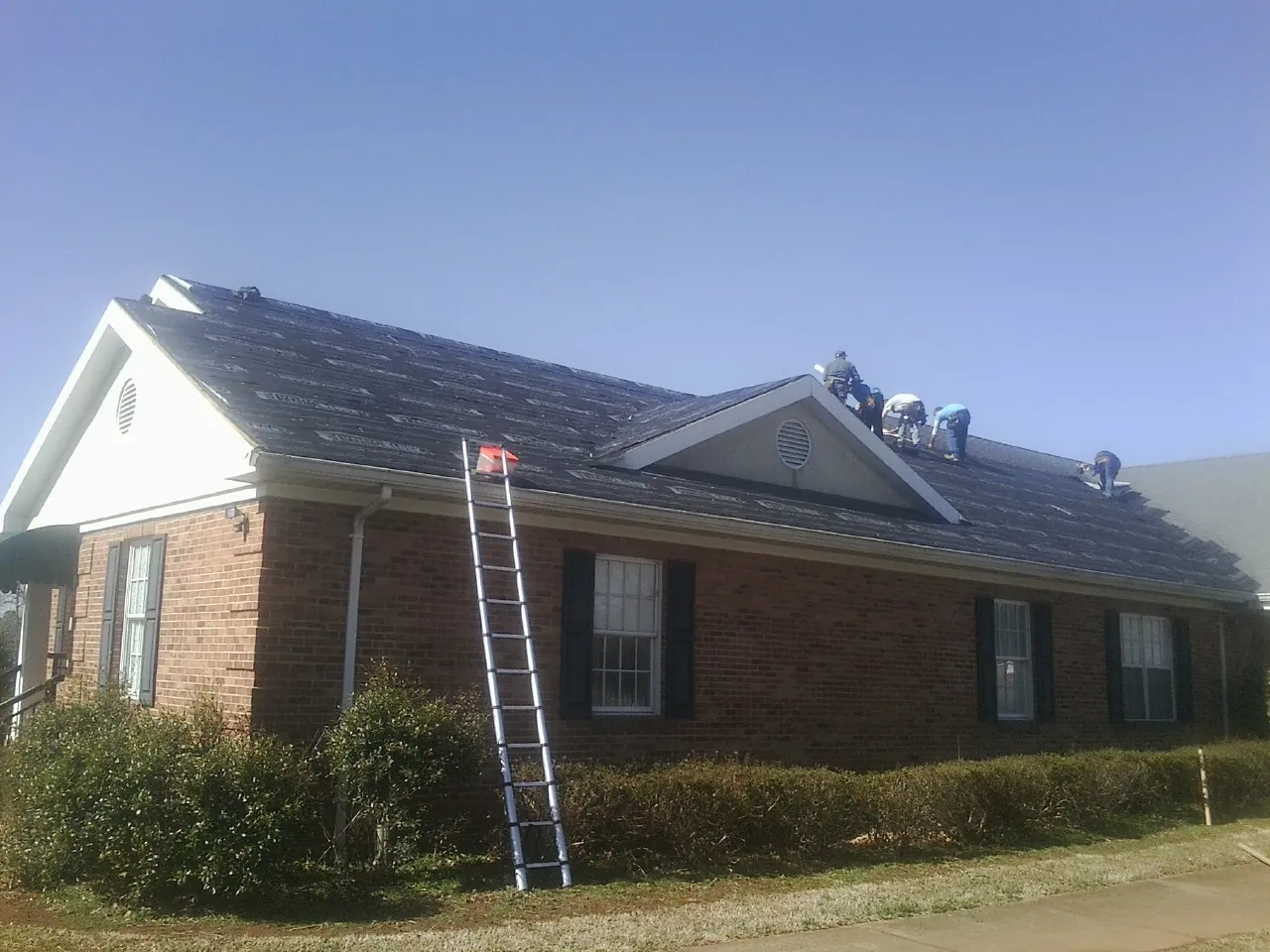 Crew tearing shingles off a brick ranch roof with a ladder set — Emergency Roof Repair work by our crew in Ethelsville