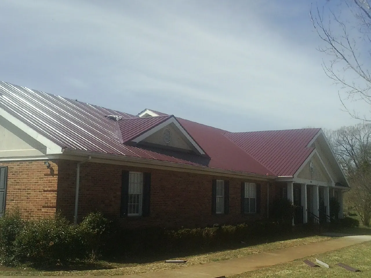 Red metal roof with gabled entries on a long brick building, from a Hail Damage Roof Repair job in Ethelsville