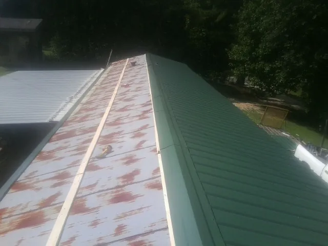 Old rusted panels beside newly installed green metal roofing — Wind Damage Roof Repair by Roofing Brothers in Ethelsville