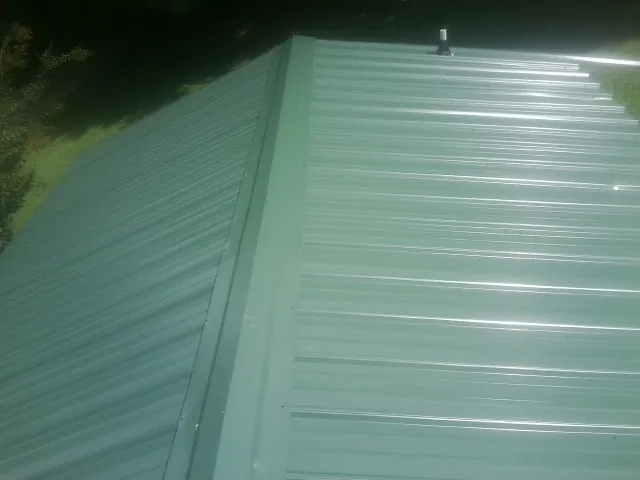 New green metal panels meeting at the ridge of a roof — Flat Roof Repair work by our crew in Ethelsville