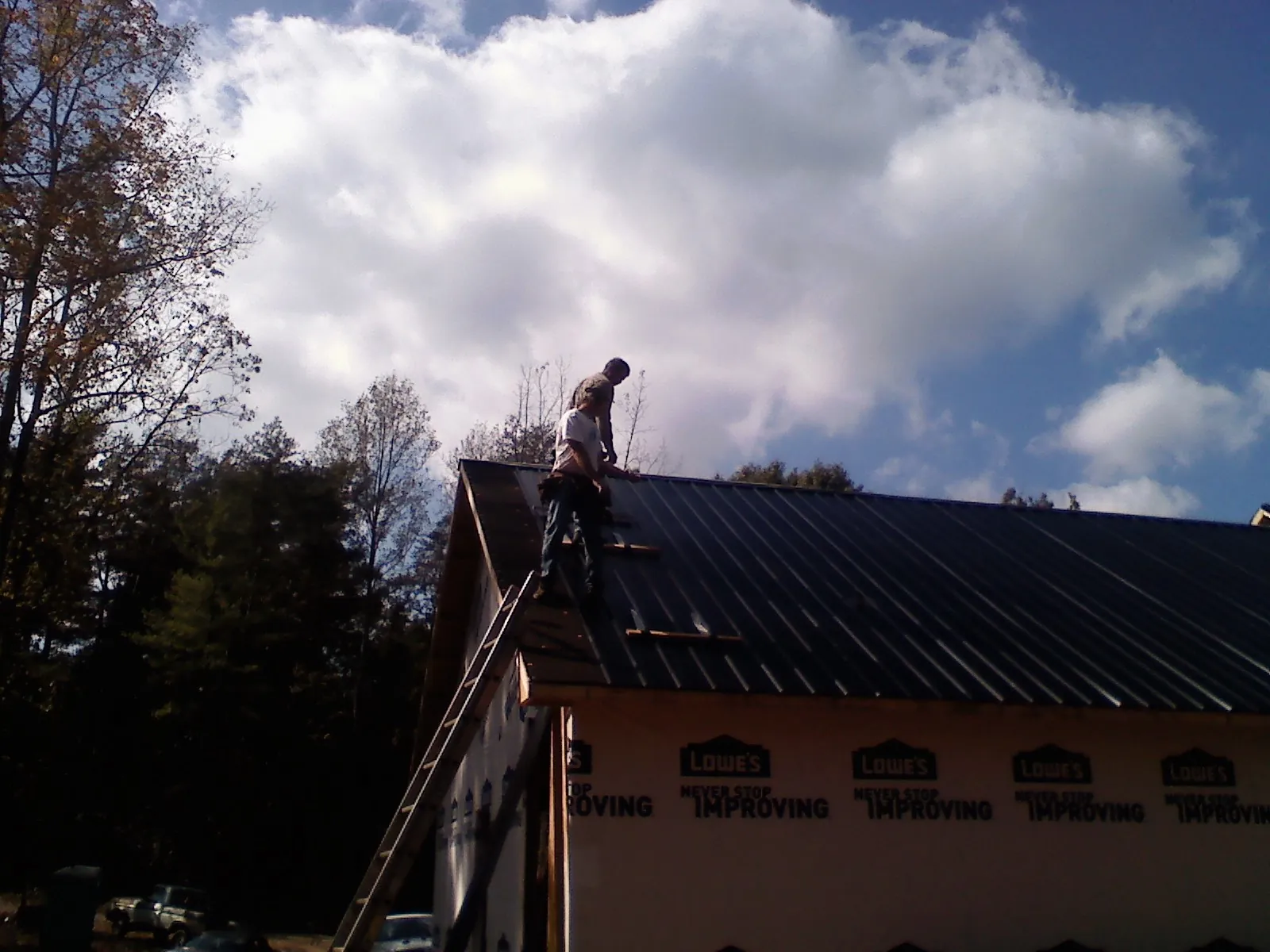 Roofer fastening dark metal panels high against a cloudy sky, from a Roof Inspection job in Ethelsville