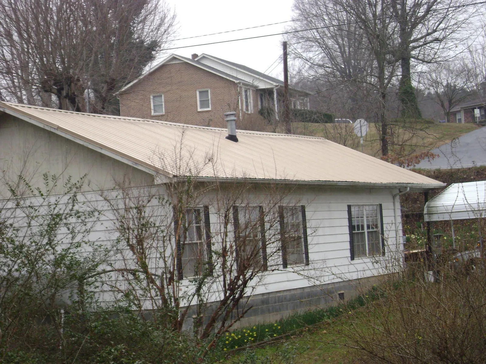 Tan metal roof on a white sided house set into a hillside — Commercial Roofing by Roofing Brothers in Ethelsville