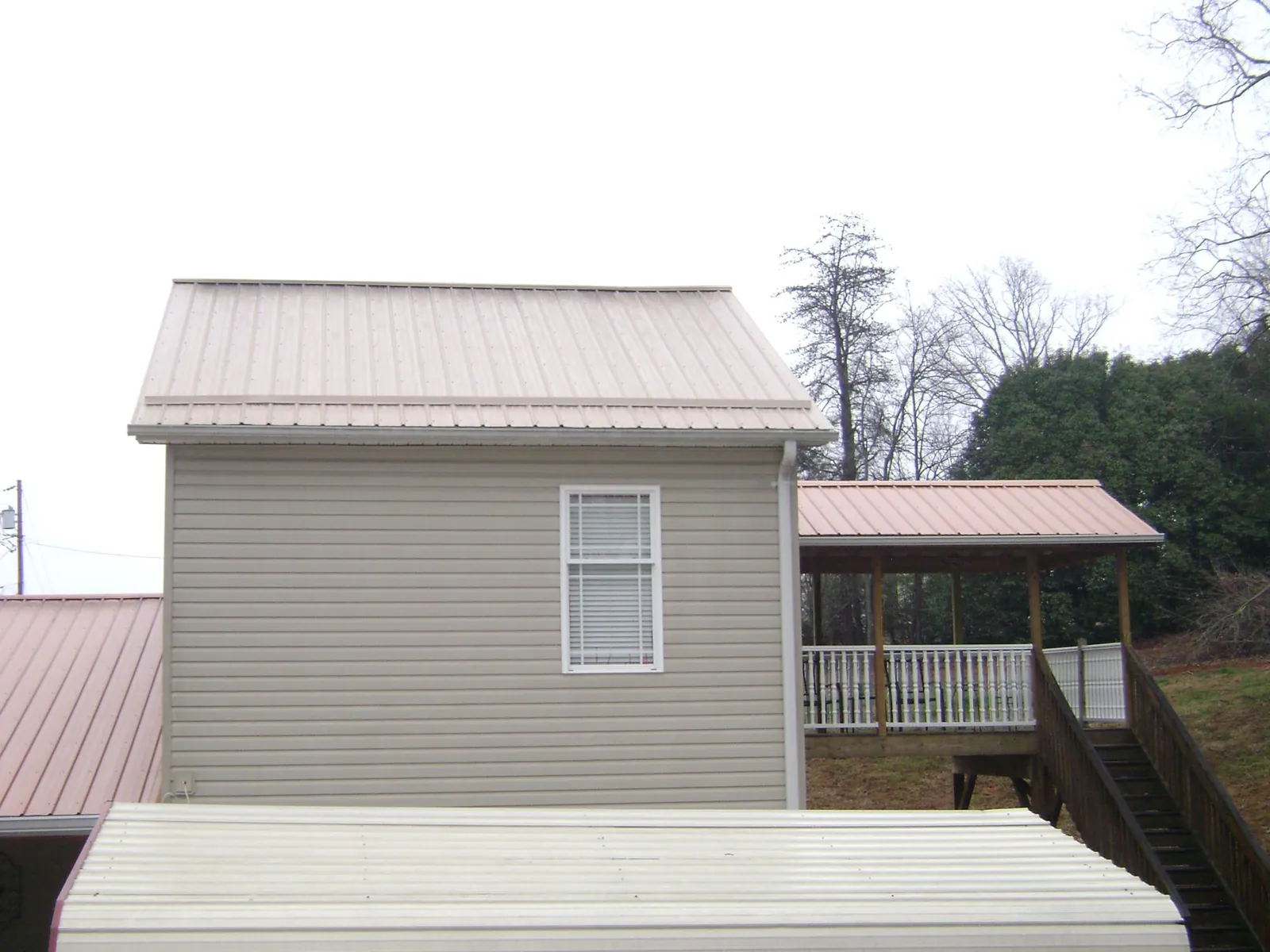 Tan metal roofs on a two story addition and attached porch, from a Roof Replacement job in Ethelsville